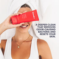 Smiling woman with a towel on her head holding the red Duradry Deep Clean Body Wash.